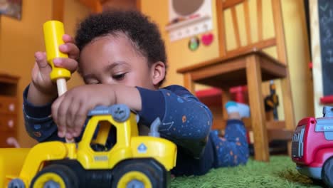 Szene-Eines-Dreijährigen-Schwarzen-Kleinkindes,-Das-Zu-Hause-Spielt,-Um-Seine-Auf-Einem-Grünen-Teppich-Liegenden-Spielsachen-Zu-Reparieren