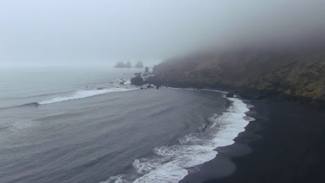 Aerial-drone-pan-right-at-Vik-Iceland-early-winter-fog-at-Black-Sand-Beach-waves-crashing-on-shore-mysterious