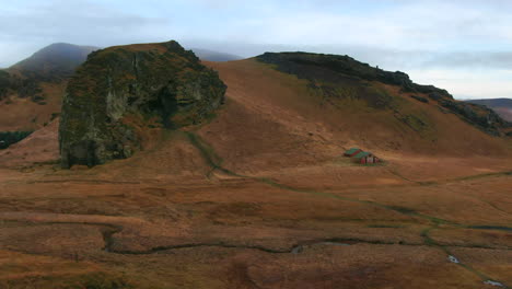 Vista-De-Drones-Con-Zoom-Inverso-De-Montañas,-Acantilados,-Pájaros-Y-Graneros-Abandonados-En-Un-Valle-En-Un-Día-Nublado-En-Islandia
