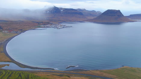 Vista-Panorámica-De-Drones-De-Una-Comunidad-Costera-En-Islandia-Con-Montañas-En-La-Distancia-Montaña-Kirkjufell-Cerca-De-Grundarfjordour
