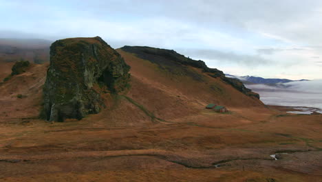 Panoramic-view-of-mountains,-cliffs,-ocean,-river-and-abandoned-barns-in-a-valley-on-a-cloudy-day-in-Iceland