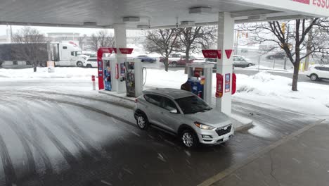 Aerial-orbit-around-car-at-gas-petrol-station-filling-tank-up-in-snow-storm-in-canada