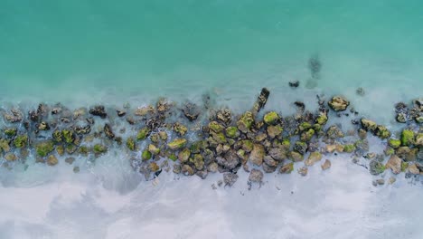 Splashing-Blue-Ocean-Water-Among-Rocks-Covered-in-Algae-Along-the-Seashore-Aerial-Crane