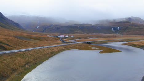 Vista-De-Drones-De-Una-Plantación-En-El-Valle,-Debajo-De-Las-Montañas-Y-Justo-Al-Lado-De-La-Orilla-De-Un-Río-En-Islandia