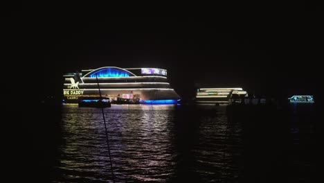Erleben-Sie-Den-Bezaubernden-Blick-Auf-Segelboote-Und-Leuchtende-Lichter,-Die-Vor-Dem-Majestätischen-Casino-über-Das-Meer-Scheinen-Und-Sie-Zu-Einem-Magischen-Spielabenteuer-Einladen
