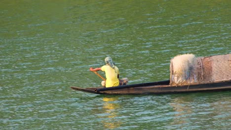 A-fisherman-paddling-on-a-traditional-wooden-boat-along-a-serene-river-in-Bangladesh,-surrounded-by-lush-greenery-and-nature