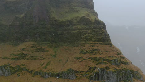 Aerial-cinematic-pan-left-and-up-drone-view-of-mountains,-cliffs-and-birds-on-an-overcast-day-Kirkjufell-Mountain-near-Grundarfjordour-Iceland
