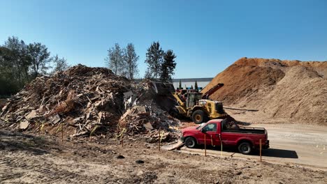 Roter-Kleintransporter-Mit-Lader,-Der-Auf-Dem-Sägewerksabfallhaufen-Auf-Dem-Recyclinggelände-Schaufelt