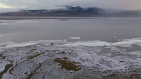 Espectacular-Vuelo-De-Fuego-Y-Hielo-Sobre-El-Mar-Y-La-Costa-Parcialmente-Congelados-Acercándose-A-Las-Nubes-Eclipsando-Una-Montaña-En-El-Fondo