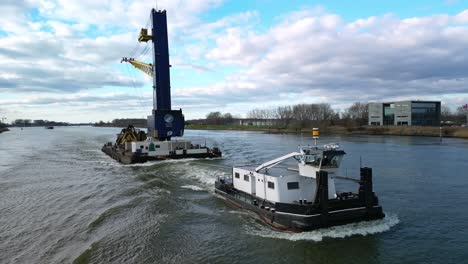 Slow-industrial-ship-with-a-crane-navigating-through-the-inland-canal,-aerial-rotating-view