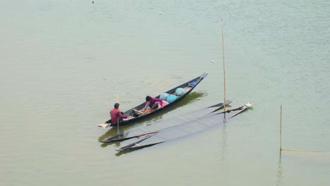 fisherman-teaches-son-how-to-catch-fish-in-wooden-boat,-old-boats-lay-sunken-by-them