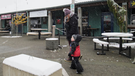 A-woman-is-enjoying-snowfall-and-walking-with-a-toddler-outside-a-market-in-British-Columbia-Canada