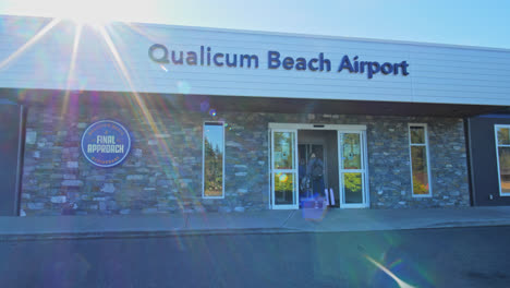 Two-people-enter-through-the-gate-of-Qualicum-Beach-Airport-while-a-car-is-passing-by-in-a-sunny-day
