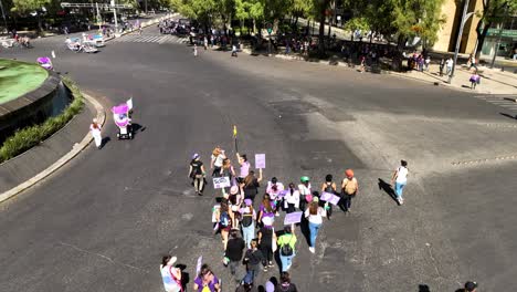 Vista-Aérea-Siguiendo-A-Una-Multitud-De-Personas-Marchando-Por-Las-Calles-De-La-Ciudad-De-México