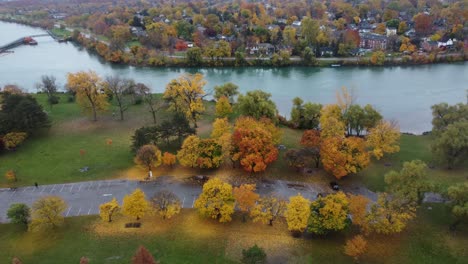 Aerial-View-Of-Car-Park-Surrounded-By-Autumn-Park-Trees-Beside-River-In-Brampton,-Canada