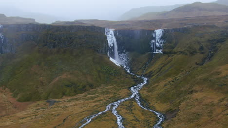 Aerial-drone-pan-up-Majestic-waterfall-cascading-into-a-canyon-and-the-water-flows-into-different-streams-in-Iceland-Kirkjufell-Mountain-near-Grundarfjordour