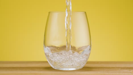 Total-view-pouring-fresh-clear-sparkling-water-in-a-drinking-glass-on-isolated