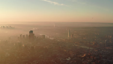 Stationary-aerial-shot-over-London-at-sunrise-as-a-plane-comes-in-to-land-at-city-airport