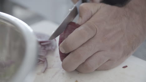Close-up-of-a-man-cutting-a-red-onion-in-slices-on-a-white-plate-in-slowmotion-LOG