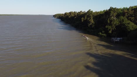 Aerial-tracking-shot-of-Small-Boat-near-river-shore-in-Argentina-during-sunny-day
