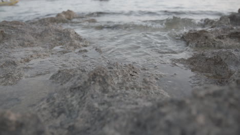 Close-up-slowmotion-shot-of-water-hitting-some-rocks-near-the-shore-and-splashingLOG