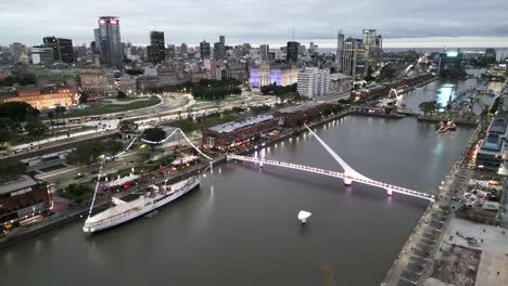 Luftdrohnen-Fliegen-über-Dem-Dock-Von-Puerto-Madero,-Der-Frauenbrücke-In-Der-Stadt-Buenos-Aires,-Argentinien,-Dem-Berühmten-Reiseziel-Wasserkanal-In-Der-Abenddämmerung
