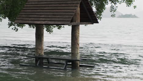 Banco-Del-Parque-Sumergido-En-Agua-De-Inundación-Por-Un-Lago-Sereno-En-Un-Día-Nublado