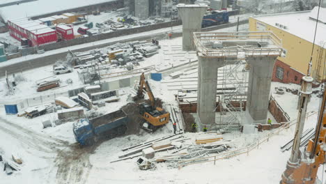 Excavator-loading-dirt-into-truck-at-bridge-construction-site-in-snow