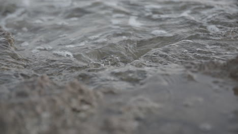 Close-up-slowmotion-shot-of-water-hitting-some-rocks-near-the-shore-and-splashingLOG