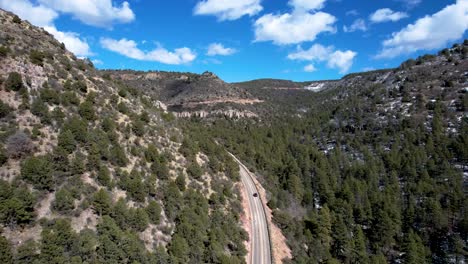 Mountain-Pass-in-high-desert-with-blue-sky-and-car-driving-through-pine-forest--aerial