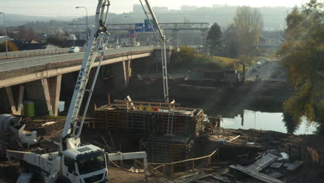 Truck-cement-pump-working-at-riverside-pipeline-dig-below-road-bridge