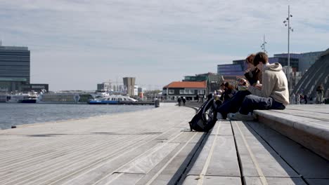 Young-people-sitting-on-boardwalk-in-cloudy-Amsterdam,-slomo-side-view