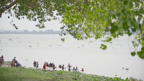 People-bathing-and-swimming-in-river-bank-of-Ganga-in-hot-summer-season,-wind-blowing,-slow-motion