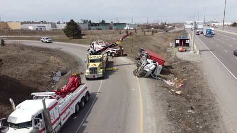 Tow-trucks-using-cranes-to-recover-tipped-over-truck-next-to-Highway-410,-drone
