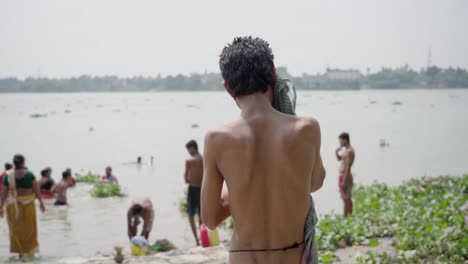 Midshot-of-man-cleaning-his-body-after-bath-in-hot-summer-season,-poor-people-bathing-in-river-bank-of-Ganga,-Rani-Rashmoni-ghat,-slow-motion