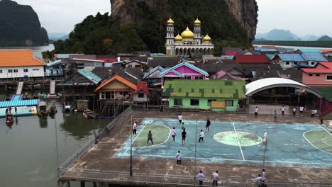 Drone-shot-toward-people-playing-soccer-at-the-Ko-Panyi-Floating-Fishing-Village,-in-cloudy-Thailand