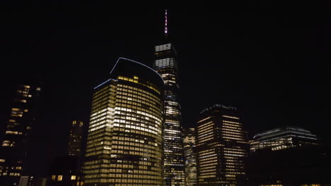 Illuminated-buildings-in-Battery-park-city,-Manhattan,-New-York,-USA---descending,-drone-shot