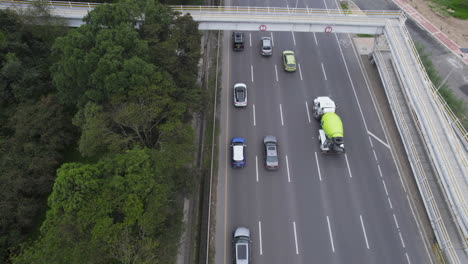 Overhead-drone-clip-following-queue-of-cars-and-truck-moving-along-fast-moving-treelined-highway-with-multiple-lanes