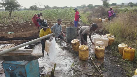 Los-Niños-Llenan-Recipientes-De-Plástico-Con-Agua-Potable-Junto-A-La-Pared-Del-Pozo-En-Loitokitok,-Kenia