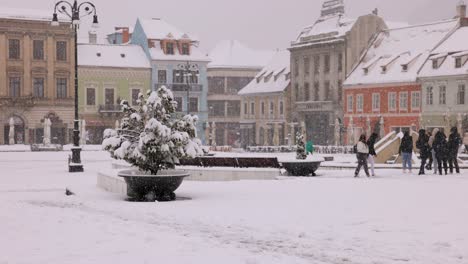 People-On-The-Main-Square-Of-The-Old-City-Of-Brasov-In-Transylvania,-Romania-During-A-Snowy-Daytime