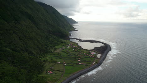 Amazing-aerial-shot-of-coastal-landscape-with-small-village-and-steep-slope-rising-from-ocean