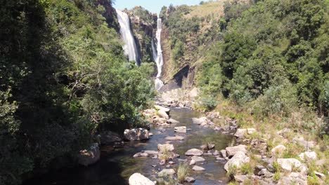 Aerial-view-following-cascading-waterfall-stream-towards-peaceful-Drakensberg-Mountain-Range