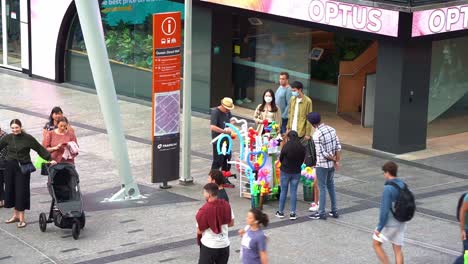 Zeitrafferaufnahme-Der-Geschäftigen-Innenstadt-Von-Brisbane,-Talentierter-Straßenmusikant,-Der-Auf-Der-Straße-Im-Queen-Street-Mall-Kunstvolle-Luftballons-Mit-Besonderer-Modellform-Verkauft