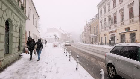 People-Walking-On-The-Side-Streets-Of-Brasov-Old-Town-During-Snowfall-In-Transylvania,-Romania