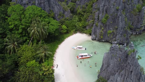 Aerial-Push-in-reveal-view-:-Tour-C-Island-Hopping-Boats-on-white-sand-of-Hidden-beach-between-Karst-Rock-formations-and-tropical-Jungle