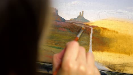 Artist-in-foreground-holds-wide-tip-paintbrush-oil-painting-desert-monument-valley-landscape
