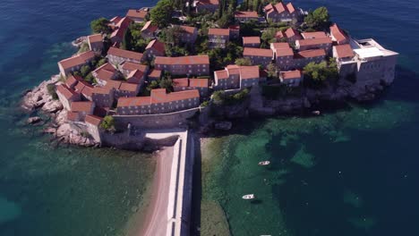 Reveal-shot-beautiful-city-of-Sveti-Stefan-in-Montenegro-surround-with-turquoise-blue-water,-aerial