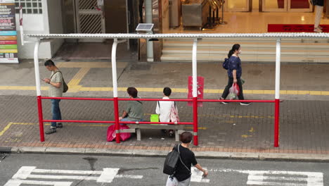 Blick-Aus-Der-Vogelperspektive-Auf-Menschen,-Die-An-Der-Bushaltestelle-Warten,-Während-Andere-Auf-Dem-Bürgersteig-In-Hongkong-Laufen