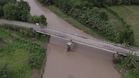Concrete-bridge-crosses-a-small-river-with-brown-water-at-Sumba-island,-aerial