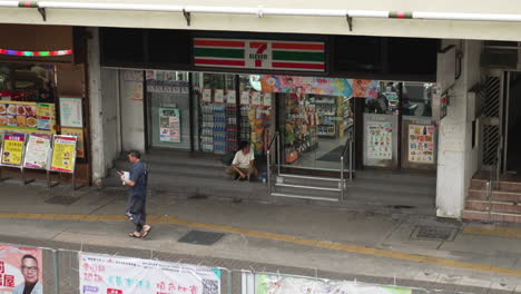 Un-Hombre-Sin-Hogar-Espera-Sentado-Afuera-Del-7-11-En-Hong-Kong,-Asia